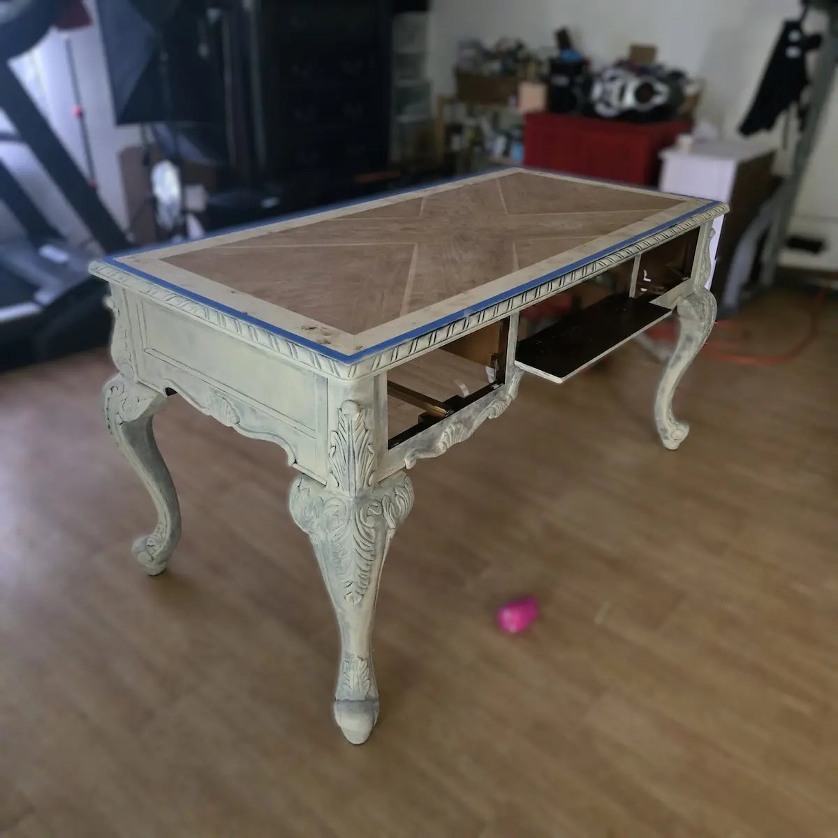 Carved desk before restoration with a pale painted base, geometric wood top, and one drawer open